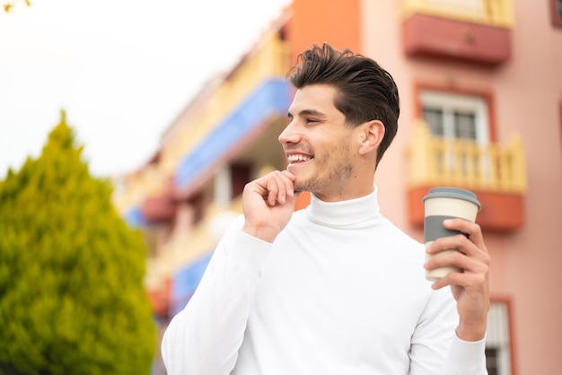 Jovem homem caucasiano segurando um café para viagem ao ar livre pensando em uma ideia e olhando de lado