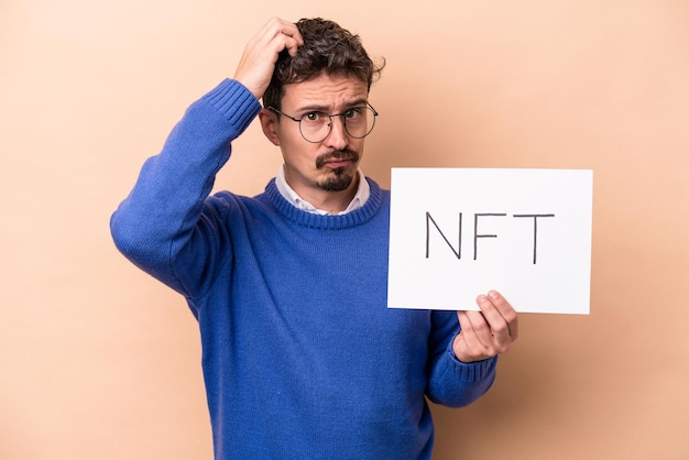 Jovem homem caucasiano segurando um cartaz nft isolado em fundo bege sendo chocado, ela se lembrou de uma reunião importante.