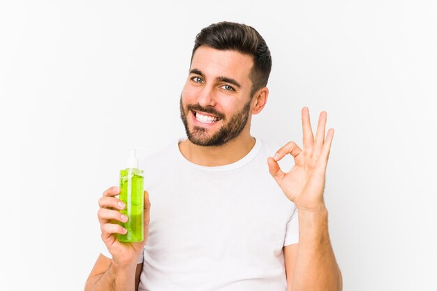 Jovem homem caucasiano segurando um creme hidratante com aloe vera alegre e confiante mostrando okey gesto.