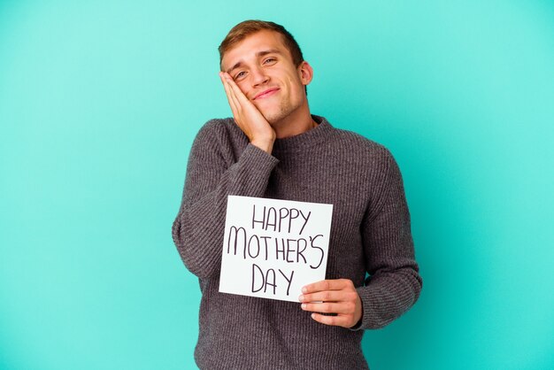 Jovem homem caucasiano segurando um feliz dia das mães isolado em fundo azul