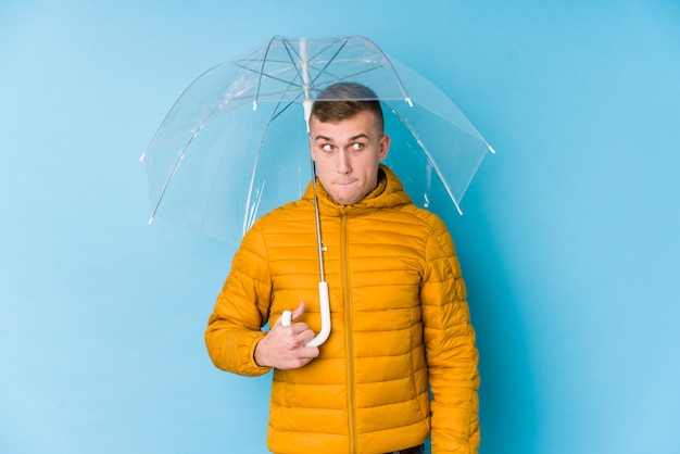 Jovem homem caucasiano segurando um guarda-chuva confuso, sente-se duvidoso e inseguro.