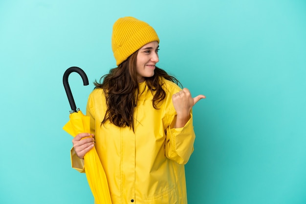 Jovem homem caucasiano segurando um guarda-chuva isolado em um fundo azul apontando para o lado para apresentar um produto