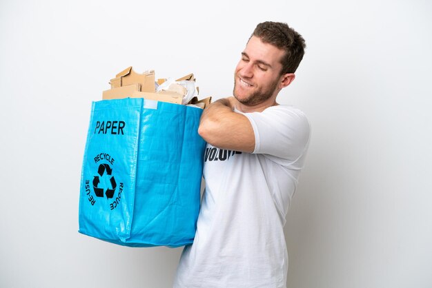 Jovem homem caucasiano segurando um saco de reciclagem cheio de papel para reciclar isolado no fundo branco, sofrendo de dor no ombro por ter feito um esforço