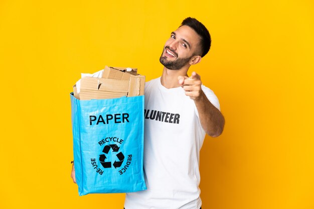 Jovem homem caucasiano segurando um saco de reciclagem cheio de papel para reciclar isolado