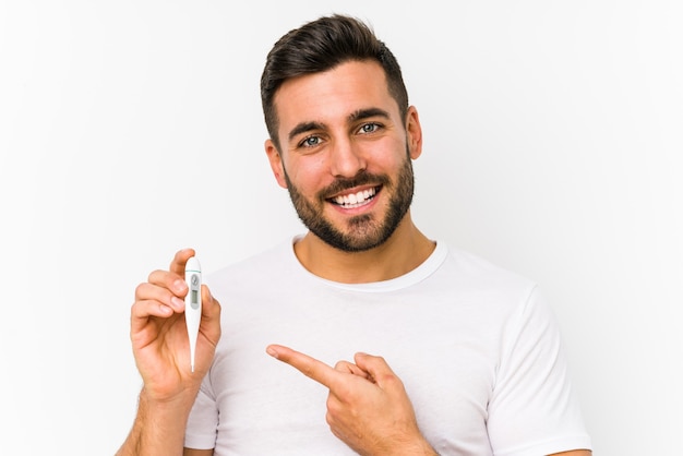 Jovem homem caucasiano segurando um termômetro isolado Jovem homem caucasiano segurando um sorriso alegremente apontando com o dedo indicador afastado.