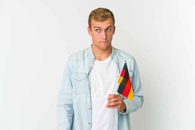 Jovem homem caucasiano segurando uma bandeira alemã isolada no fundo branco, mostrando um gesto de decepção com o dedo indicador.