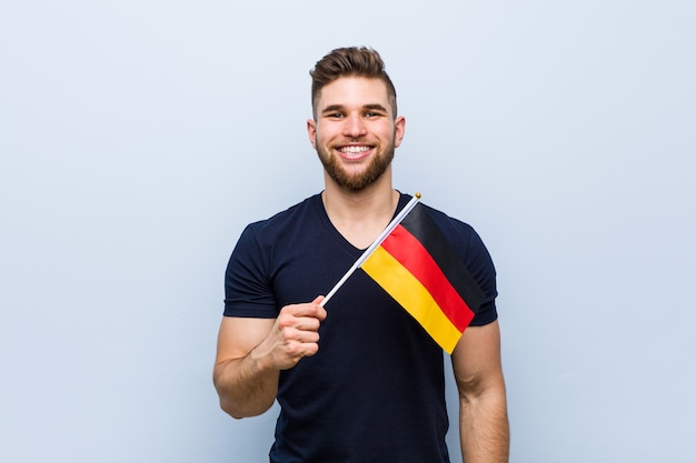 Jovem homem caucasiano segurando uma bandeira da Alemanha, feliz, sorridente e alegre.