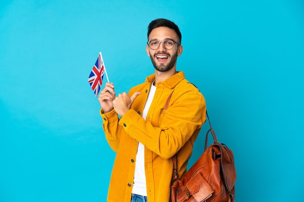 Jovem homem caucasiano segurando uma bandeira do Reino Unido isolada na parede amarela orgulhoso e satisfeito
