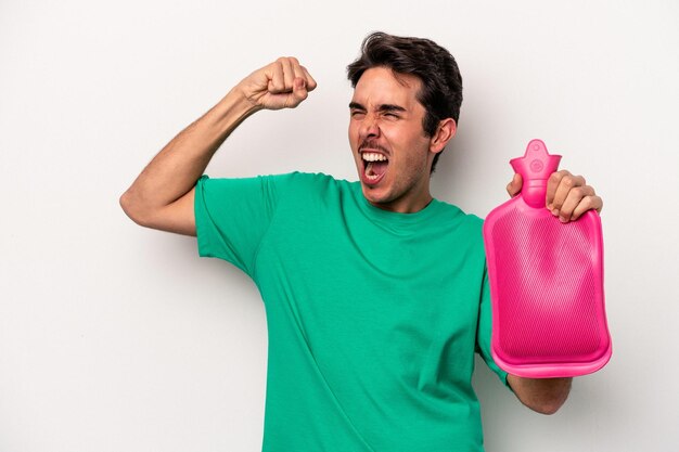 Jovem homem caucasiano segurando uma bolsa de água isolada no fundo branco, levantando o punho após um conceito de vencedor da vitória