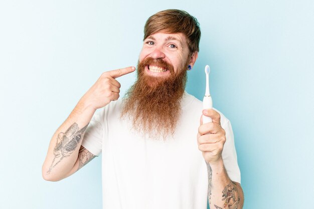 Jovem homem caucasiano segurando uma escova de dentes elétrica isolada em fundo azul