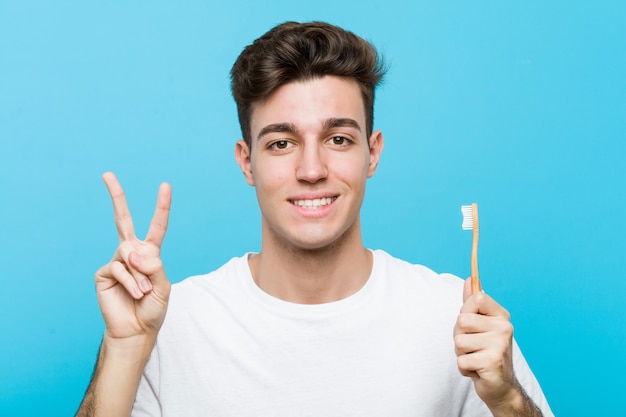 Jovem homem caucasiano segurando uma escova de dentes Jovem indiana vestindo pijama e máscara de dormir isolada segurando um travesseiro mostrando o número dois com os dedos. <Mixto>