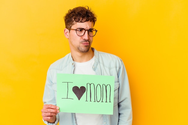 Jovem homem caucasiano segurando uma nota com o texto: Eu amo a mãe. Feliz Dia das Mães