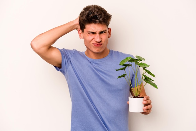 Jovem homem caucasiano segurando uma planta isolada no fundo branco sendo chocado, ela se lembrou de uma reunião importante