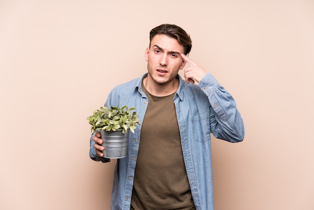 Jovem homem caucasiano segurando uma planta, mostrando um gesto de decepção com o dedo indicador.