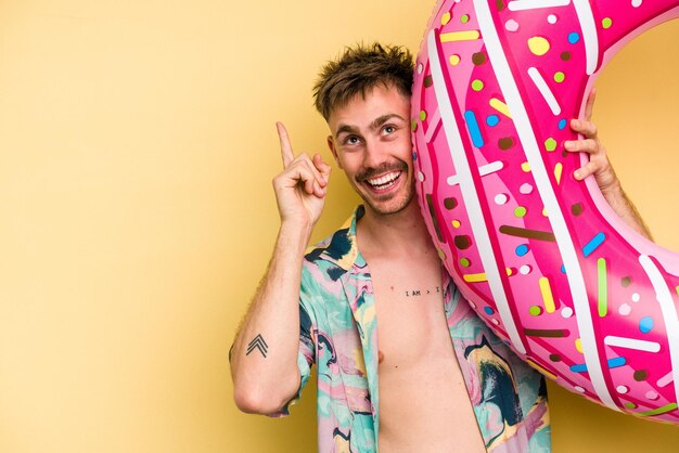 Foto jovem homem caucasiano segurando uma rosquinha inflável isolada em fundo amarelo