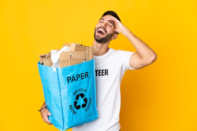 Jovem homem caucasiano segurando uma sacola cheia de papel para reciclar isolado na parede branca sorrindo muito