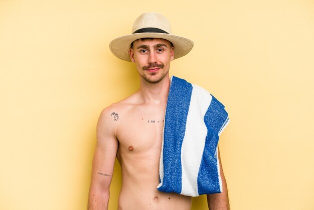 Jovem homem caucasiano segurando uma toalha isolada em fundo amarelo