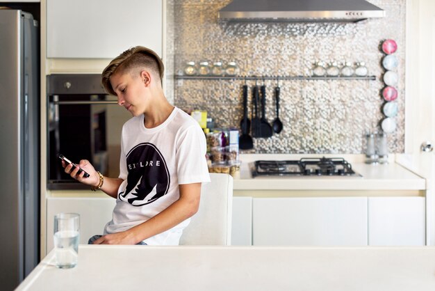 Jovem homem caucasiano sentado na cozinha usando telefone celular