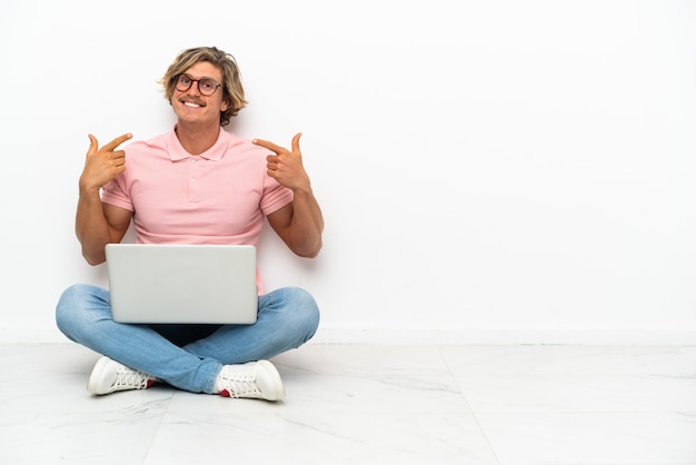 Jovem homem caucasiano sentado no chão com seu laptop isolado no fundo branco fazendo um gesto de polegar para cima