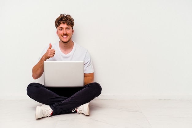 Jovem homem caucasiano sentado no chão segurando laptop isolado na parede branca Jovem homem caucasiano esporte isolado na parede azul sorrindo e levantando o polegar