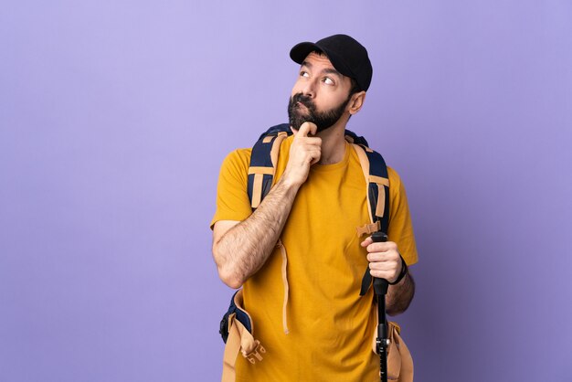 Jovem homem caucasiano sobre fundo roxo isolado, segurando os pólos de trekking