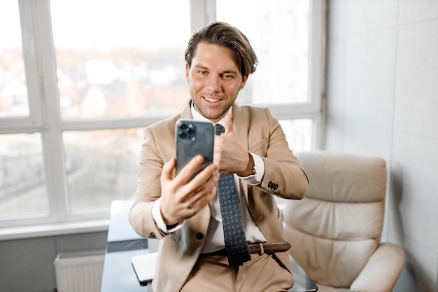 Jovem homem caucasiano sorridente usando smartphone trabalhando e reunião de videoconferência no escritório em casa