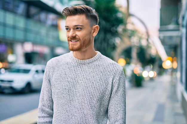 Jovem homem caucasiano sorrindo feliz em pé na cidade