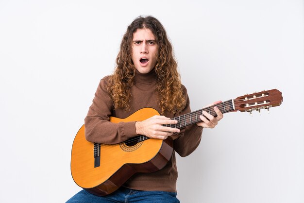 Jovem homem caucasiano tocando guitarra isolada, gritando com muita raiva e agressividade.