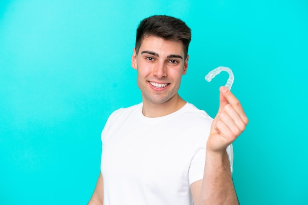 Jovem homem caucasiano usando aparelho invisível isolado em fundo azul com expressão feliz