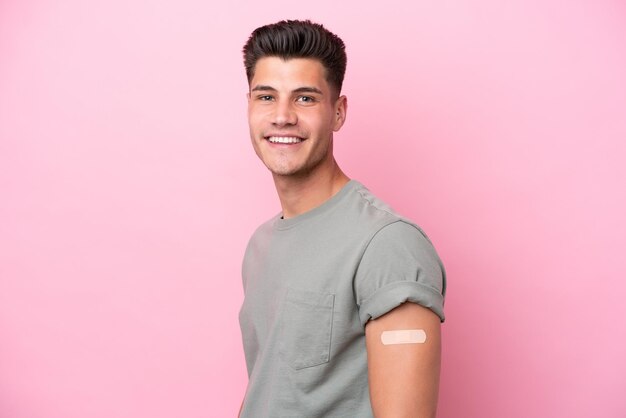 Jovem homem caucasiano usando bandaids isolados em fundo rosa com expressão feliz