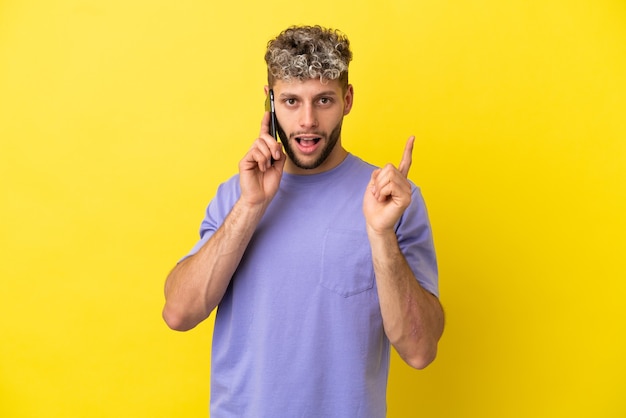 Jovem homem caucasiano usando telefone celular isolado em um fundo amarelo com a intenção de perceber a solução enquanto levanta um dedo