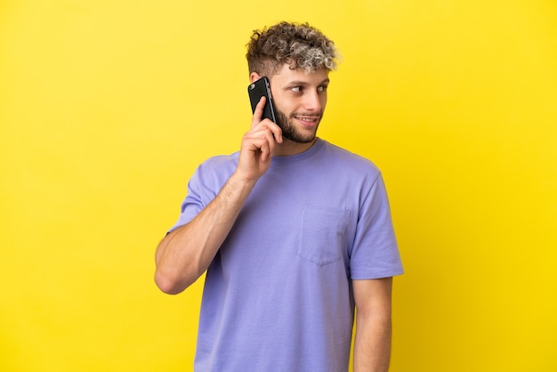 Jovem homem caucasiano usando telefone celular isolado em um fundo amarelo, olhando para o lado