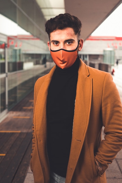 Jovem homem caucasiano usando uma máscara marrom com um casaco marrom na rua