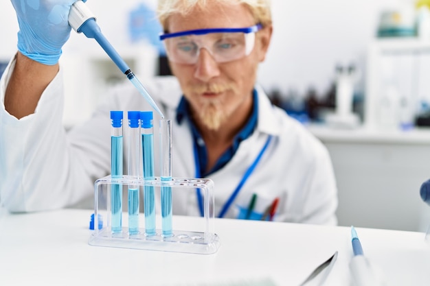 Jovem homem caucasiano vestindo uniforme de cientista usando pipeta no laboratório