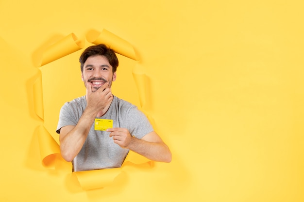 jovem homem com cartão de crédito em fundo de papel amarelo rasgado, venda de dinheiro do banco de compras