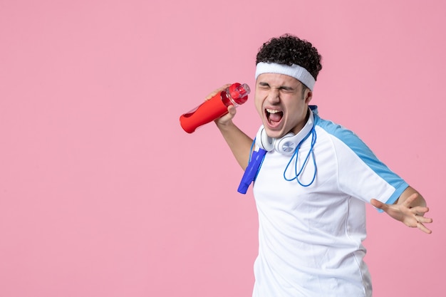 Foto jovem homem com roupas esportivas, pular corda e parede rosa de água de frente