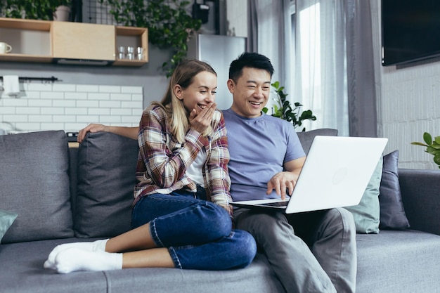 Jovem homem de família e mulher se divertindo e feliz sentado em casa usando laptop e sorrindo casal multirracial