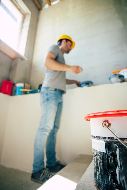 Jovem homem de reparos domésticos ou trabalhador ocupado com a reforma da casa, guarda equipamentos de construção, usa roupas de trabalho casuais na nova construção