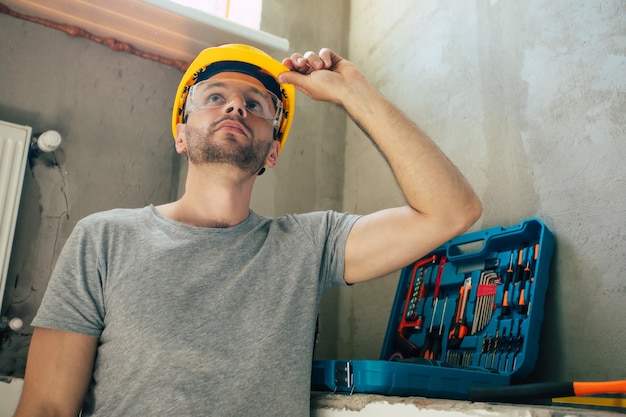 Jovem homem de reparos domésticos ou trabalhador ocupado com a reforma da casa, guarda equipamentos de construção, usa roupas de trabalho casuais na nova construção