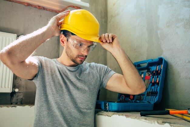 Jovem homem de reparos domésticos ou trabalhador ocupado com a reforma da casa, guarda equipamentos de construção, usa roupas de trabalho casuais na nova construção