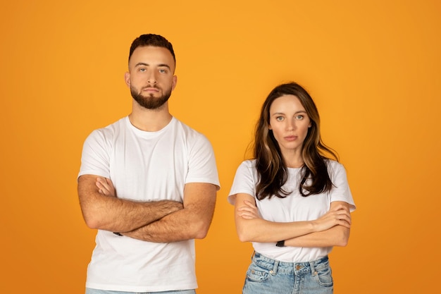 Jovem homem e mulher sérios e confiantes com camisas brancas e braços cruzados.