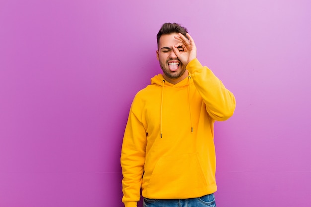 Jovem homem hispânico com look casual contra fundo roxo