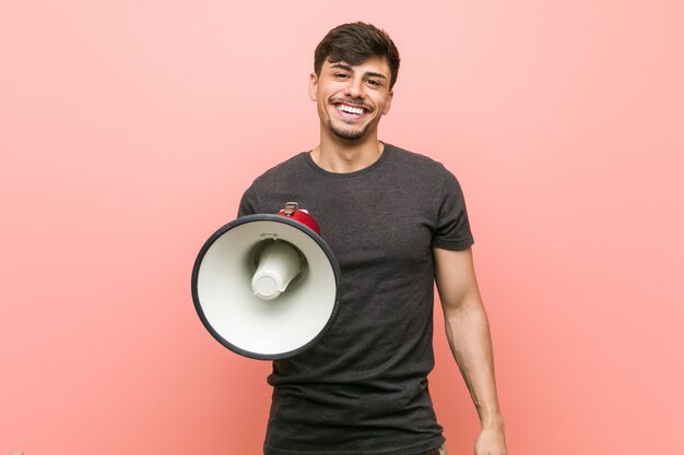 Jovem homem hispânico, segurando um megafone feliz, sorridente e alegre