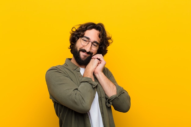 Jovem homem louco se sentindo apaixonado e bonito, adorável e feliz, sorrindo romanticamente com as mãos ao lado de enfrentar a parede amarela