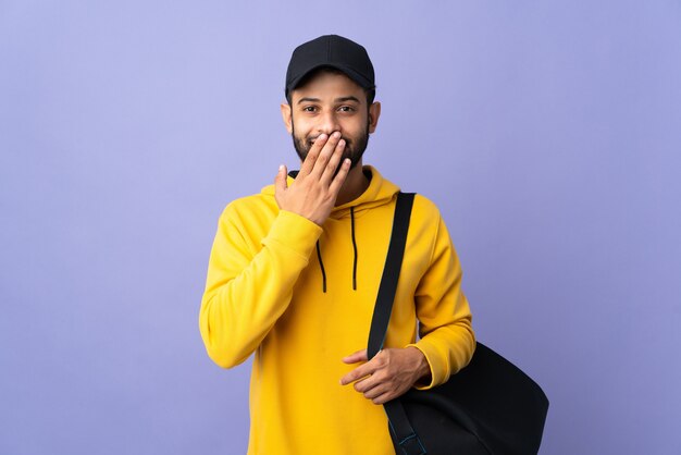 Jovem homem marroquino com bolsa esporte isolada em roxo feliz e sorridente boca coning com a mão