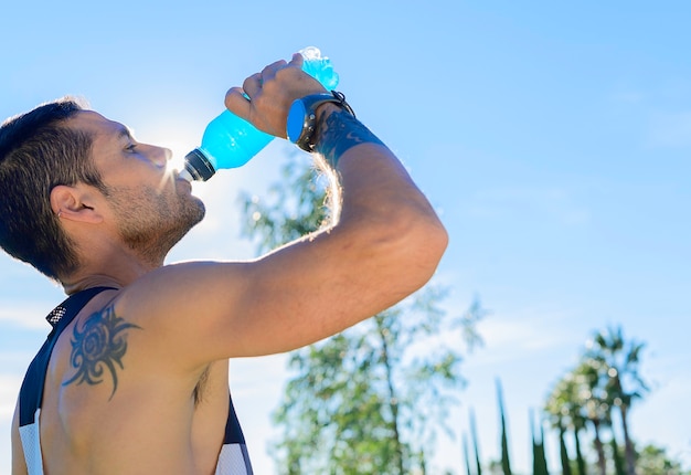 Foto jovem homem musculoso bebendo bebida isotônica depois de correr