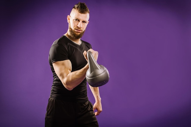 Jovem homem musculoso fazendo exercícios com peso no fundo roxo do estúdio. Copiar espaço