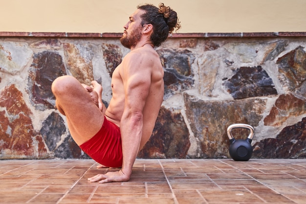Jovem homem musculoso fazendo exercícios de ioga em casa. Conceito de treinamento em casa e vida saudável.