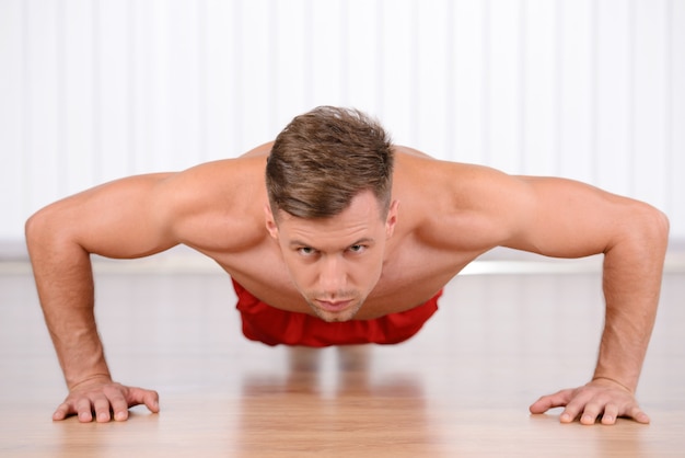 Jovem homem musculoso fazendo flexões e olhando para a câmera