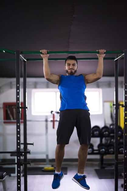 jovem homem musculoso fazendo pull ups na barra horizontal como parte do Cross Fitness Training